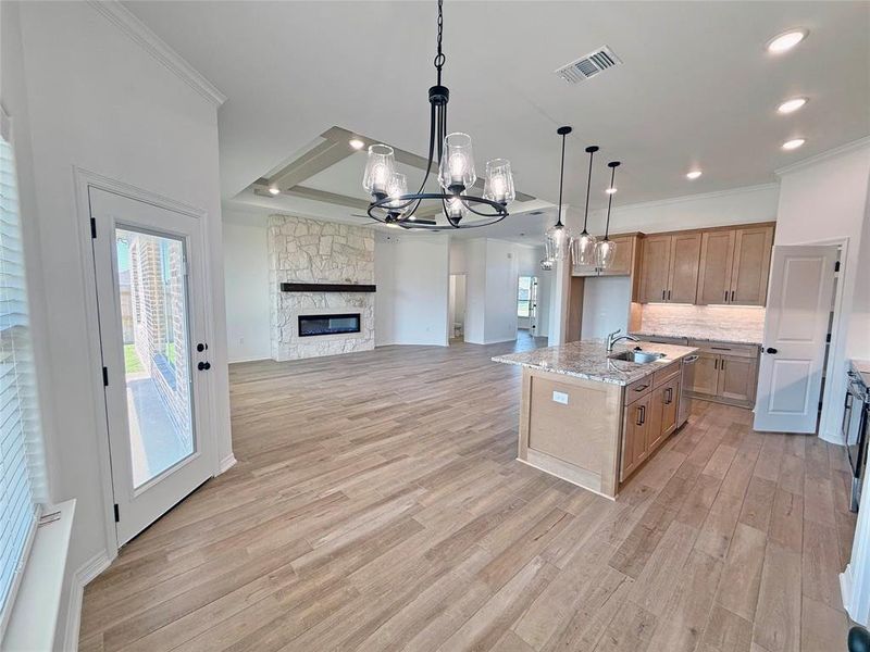 Kitchen with a chandelier, hanging light fixtures, light stone countertops, an island with sink, and open floor plan