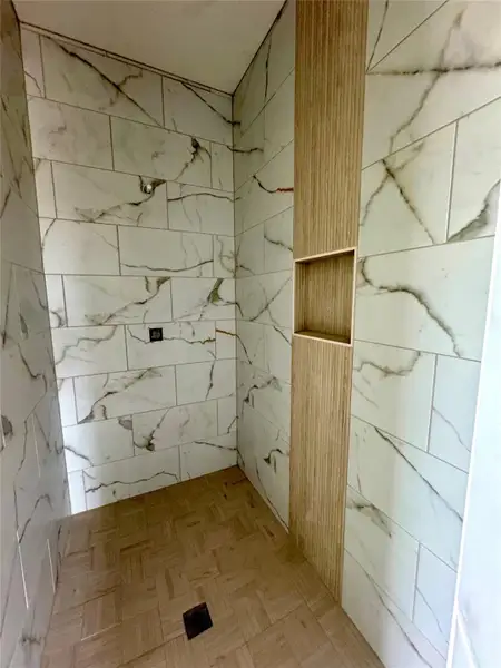 A striking shower design showcases a niche within wood-look wall panels and white marble-style tiles.