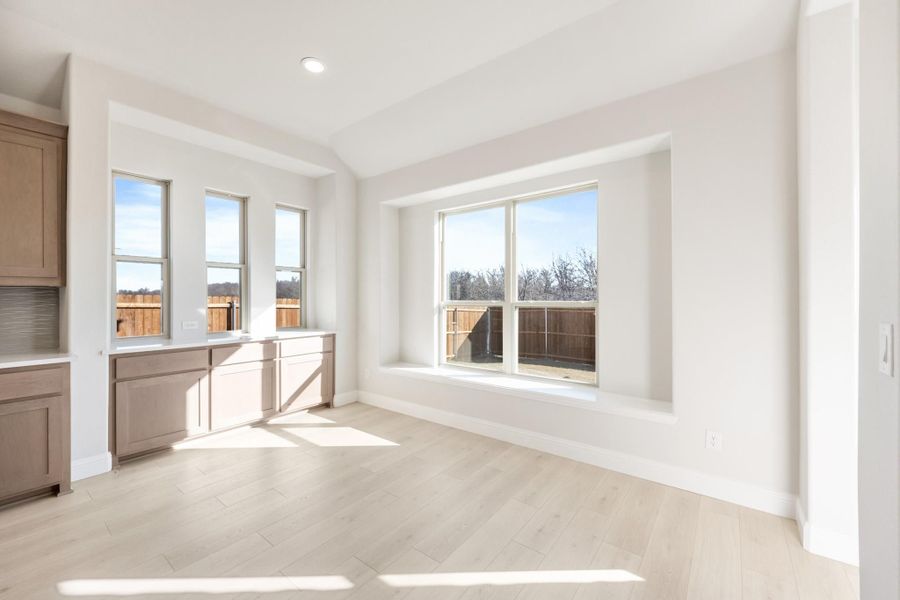 Bright dining area with light wood floors, large windows, and tan cabinetry along one wall