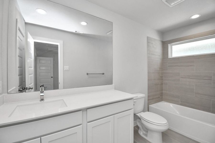 Secondary bath features tile flooring, bath/shower combo with tile surround, light stained wood cabinets, beautiful light countertop.