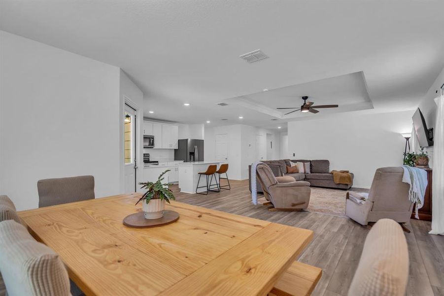 Dining space with a raised ceiling, light wood-style floors, recessed lighting, and a ceiling fan