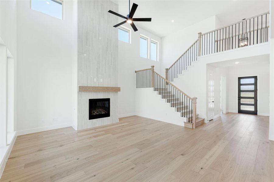 Open living room with two-story ceiling, tile fireplace, hardwood floors, and staircase leading to second floor balcony.