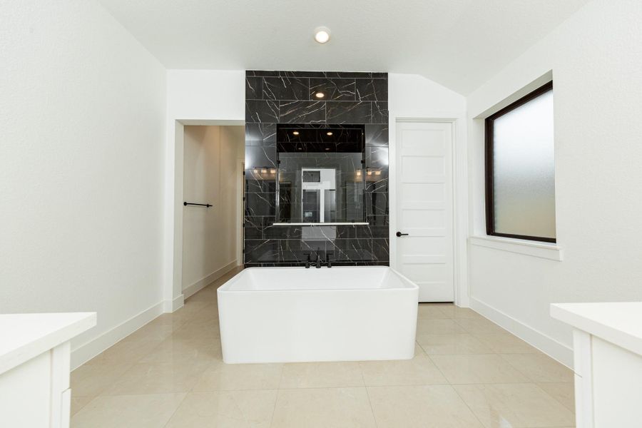 The centerpiece of this contemporary primary bath is the deep, freestanding bathtub with gorgeous black marble tile, offering an ideal spot for relaxation with a unique view into the walk-in shower.