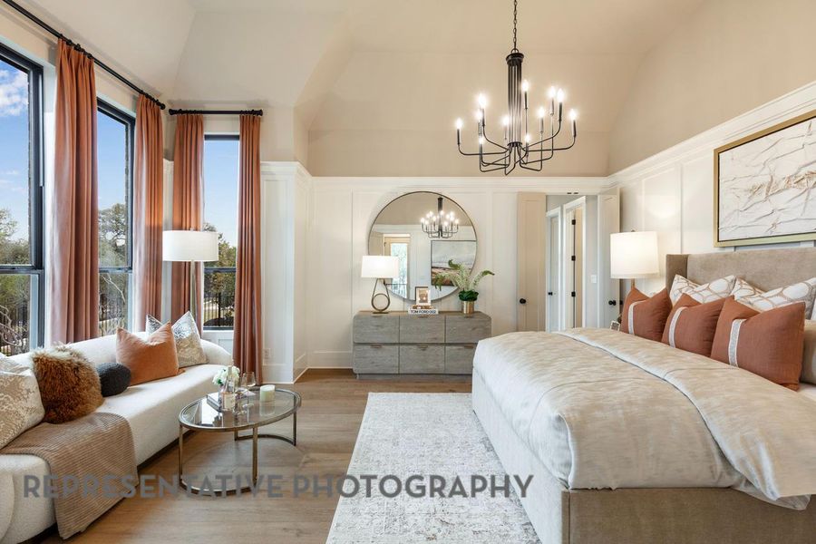 Bedroom featuring an inviting chandelier, lofted ceiling, a decorative wall, and light wood-type flooring Bedroom featuring an inviting chandelier, lofted ceiling, a decorative wall, and light wood-type flooring