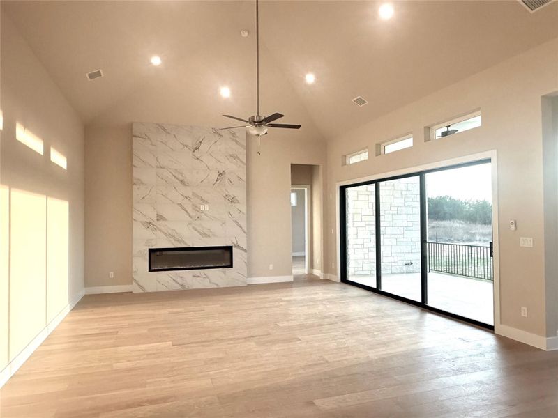 Unfurnished living room with high vaulted ceiling, light wood-style floors, a premium fireplace, ceiling fan, and recessed lighting