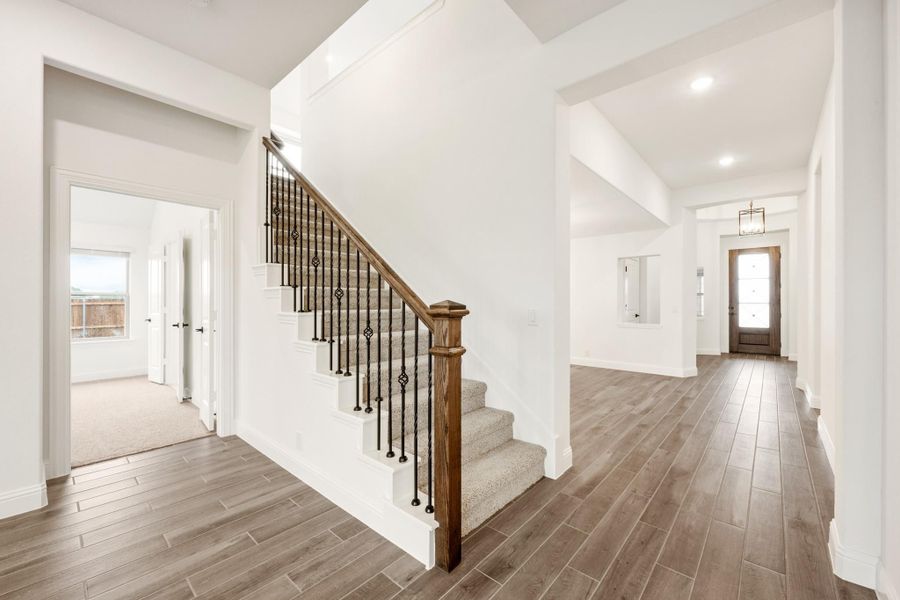 Entryway with carpeted staircase, wood railing, iron balusters, and hardwood floors leading to front door