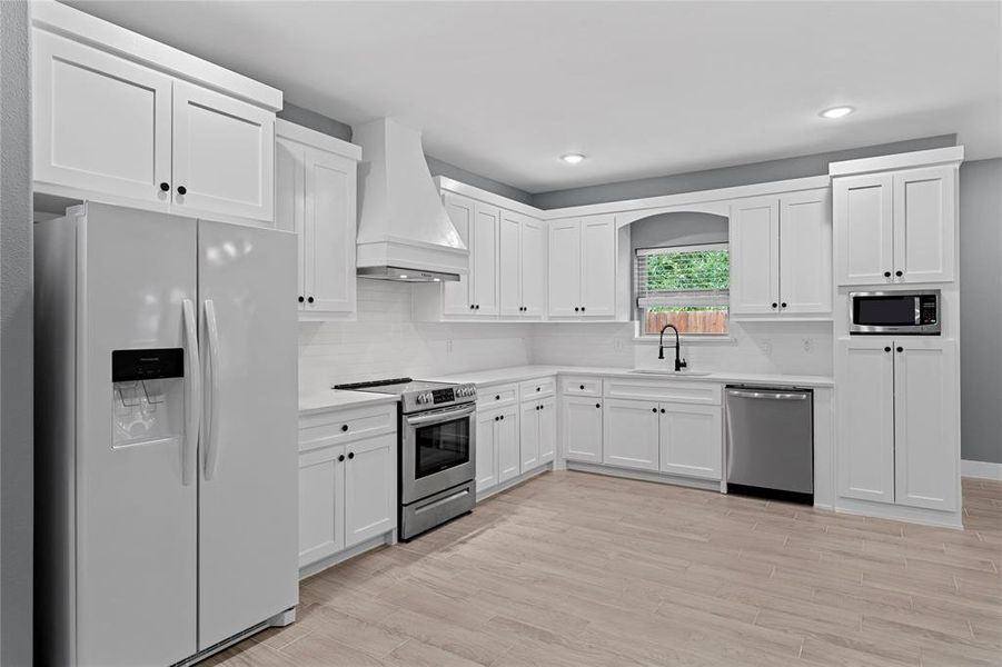 Kitchen featuring stainless steel appliances, custom exhaust hood, white cabinets, decorative backsplash, and recessed lighting Kitchen featuring stainless steel appliances, custom exhaust hood, white cabinets, decorative backsplash, and recessed lighting