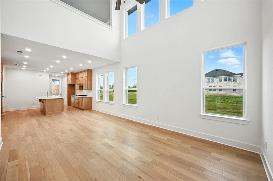 Unfurnished living room featuring light wood-type flooring and a towering ceiling Unfurnished living room featuring light wood-type flooring and a towering ceiling