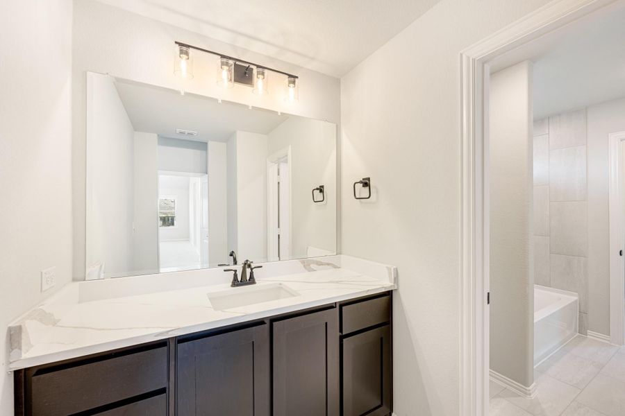 Bathroom with dark wood vanity, white quartz countertop, large mirror, and separate soaking tub visible through doorway Bathroom with dark wood vanity, white quartz countertop, large mirror, and separate soaking tub visible through doorway