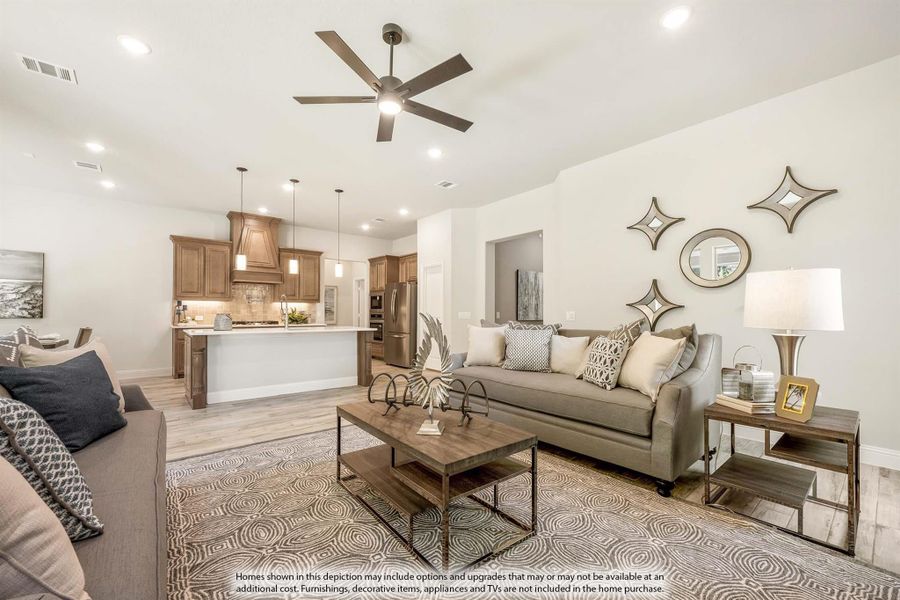 Open-concept living room with gray sofa and ceiling fan, open to kitchen with wood cabinets and island Open-concept living room with gray sofa and ceiling fan, open to kitchen with wood cabinets and island
