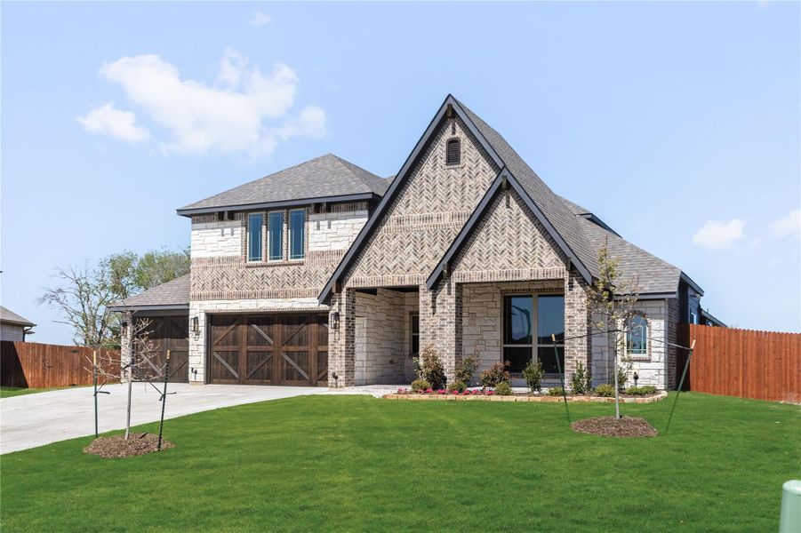 Two-story brick and stone home with two-car garage, covered entry, and green front lawn