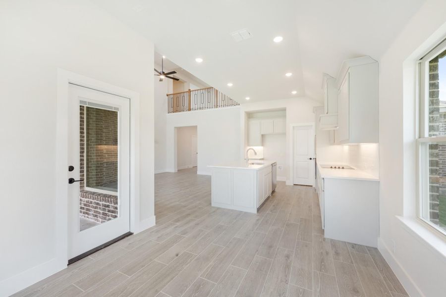 Open kitchen with white cabinets, center island, light wood-look tile floors, and second-floor loft railing visible above.