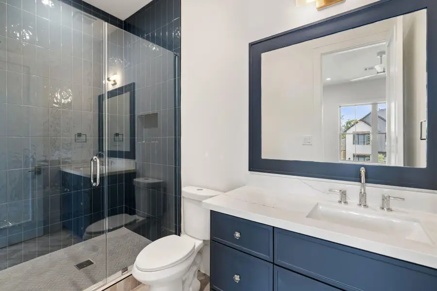 A well-appointed secondary bath features a sleek vanity with ample storage, a large mirror, and a glass-enclosed shower with full-height tile surround. Crisp finishes and a clean layout offer both style and functionality.