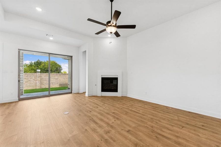 Unfurnished living room featuring light wood finished floors, ceiling fan, a glass covered fireplace, and recessed lighting Unfurnished living room featuring light wood finished floors, ceiling fan, a glass covered fireplace, and recessed lighting