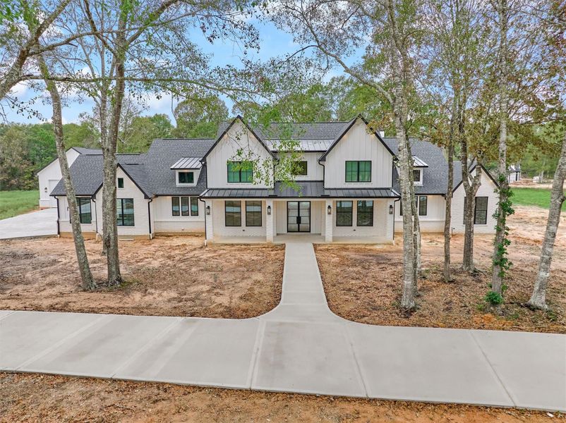 Striking modern farmhouse exterior with bold rooflines, black-framed windows, and a welcoming covered entry set against a serene wooded backdrop.