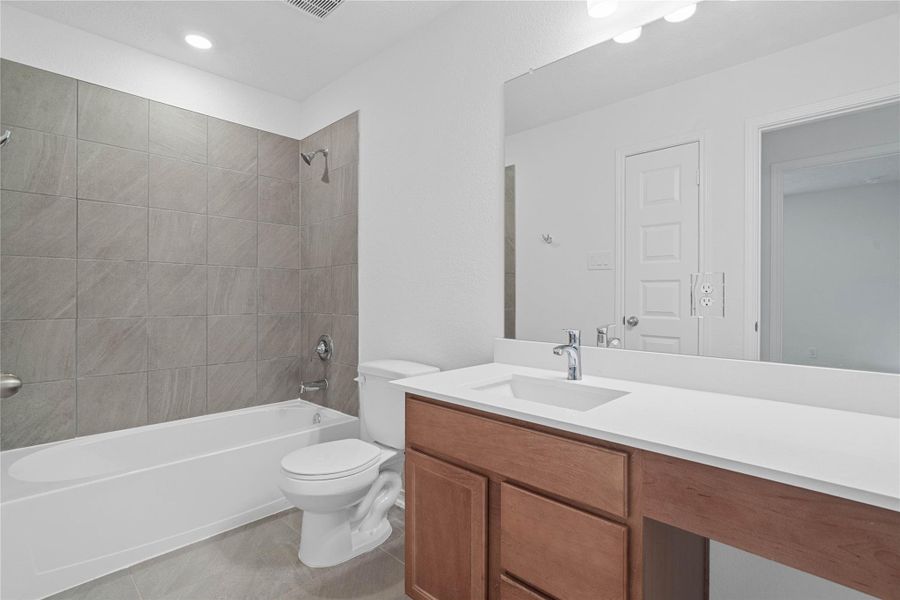 Full secondary bath featuring a rich wood vanity, crisp white countertop, and modern tile surround for the tub and shower combo.