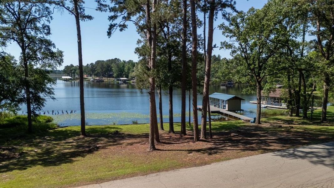 Lakefront property featuring a private boat dock with covered slip, mature trees, and a paved road frontage