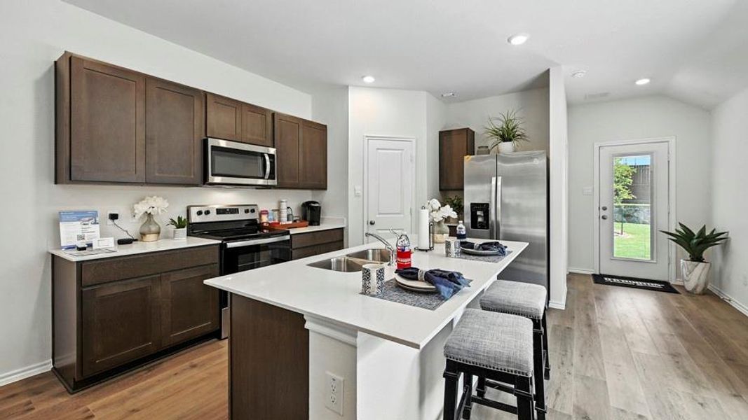 Modern kitchen featuring dark wood-finish cabinetry, white solid surface countertops, stainless steel appliances, and wood-finish flooring