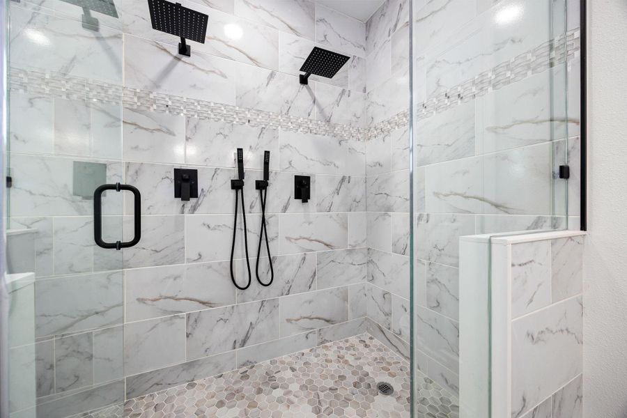 Indulge in a luxurious primary bathroom featuring elegant marble tile, dual rainfall showerheads, and sleek matte black fixtures. Indulge in a luxurious primary bathroom featuring elegant marble tile, dual rainfall showerheads, and sleek matte black fixtures.