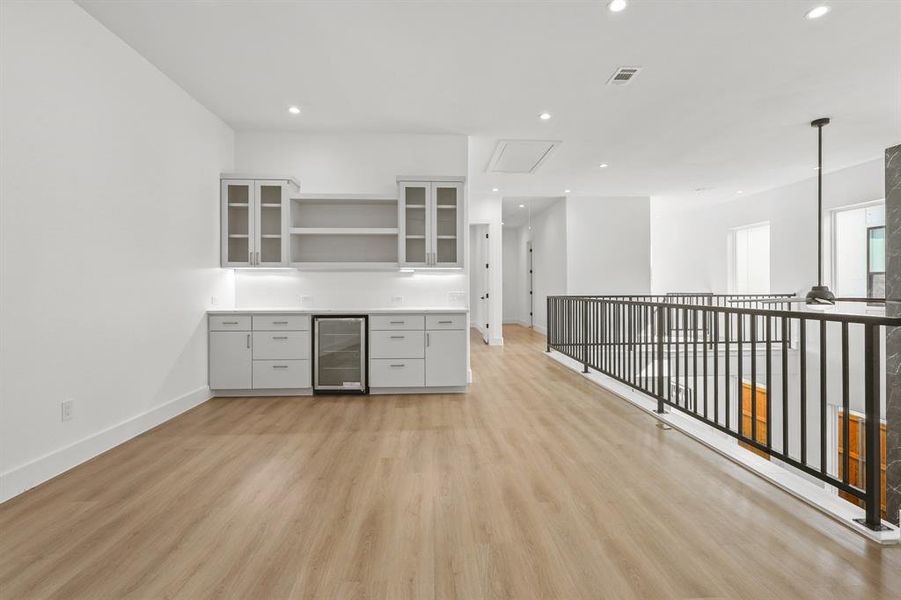 Kitchen with decorative light fixtures, gray cabinets, light wood-type flooring, and beverage cooler