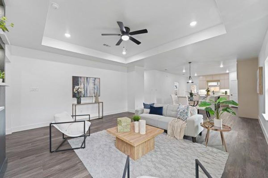 Spacious living area featuring wood-finish flooring, a tray ceiling with recessed lighting and a ceiling fan, and an open layout to the kitchen Spacious living area featuring wood-finish flooring, a tray ceiling with recessed lighting and a ceiling fan, and an open layout to the kitchen