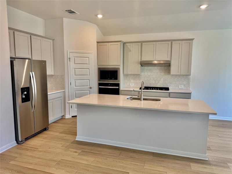 Kitchen featuring stainless steel appliances, light stone counters, decorative backsplash, light wood-style flooring, and vaulted ceiling Kitchen featuring stainless steel appliances, light stone counters, decorative backsplash, light wood-style flooring, and vaulted ceiling