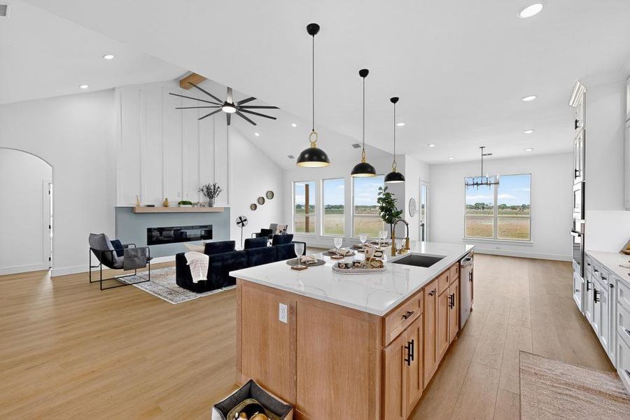 Kitchen with light wood finished floors, arched walkways, an island with sink, light stone countertops, and recessed lighting