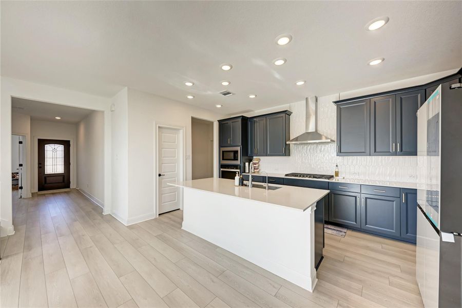 Contemporary kitchen featuring dark blue cabinetry, light wood-finish flooring, and a white countertop island