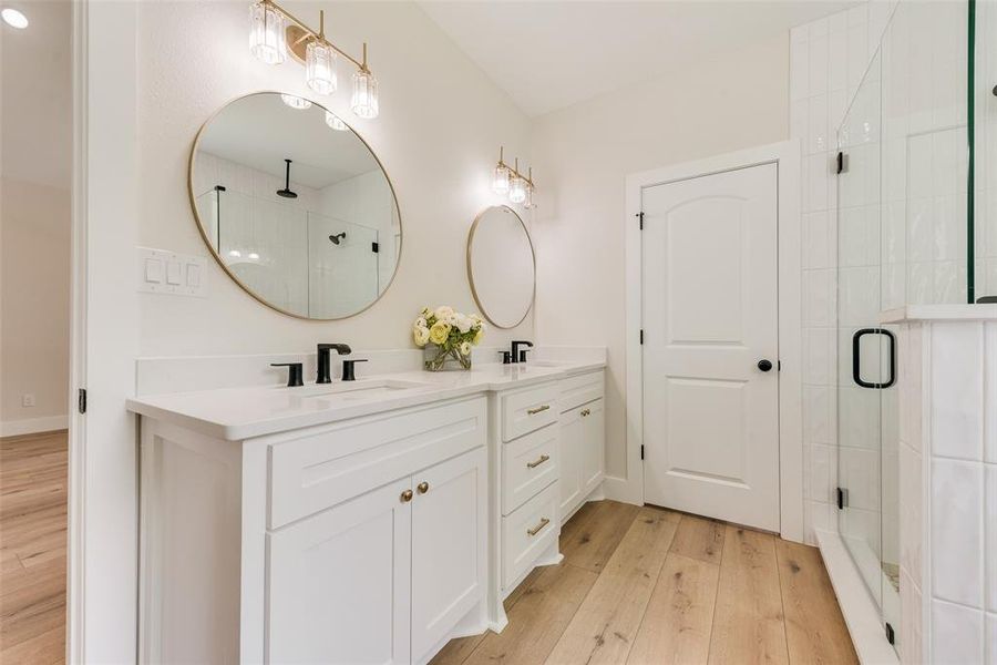 Bathroom featuring dual vanities with white cabinetry, white countertops, and circular gold-framed mirrors
