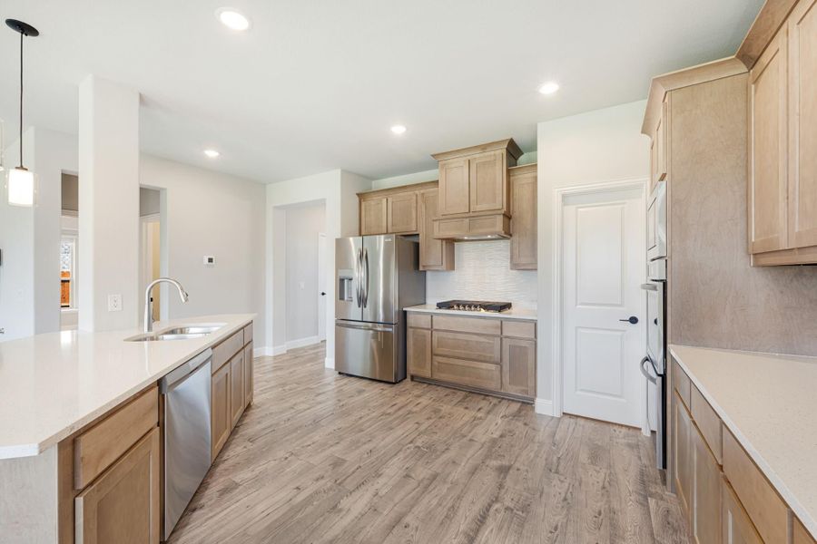 Kitchen with light wood cabinets, stainless steel appliances, white countertops, and light hardwood floors