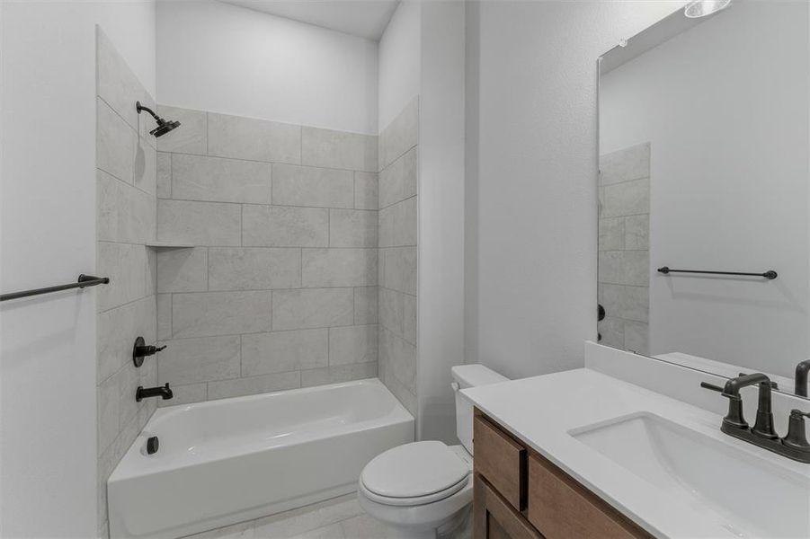 Bathroom featuring a white tub and shower combination with light-toned tiled surround, an integrated shower niche, and matte black fixtures
