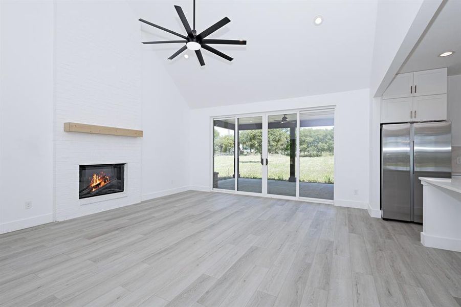 Unfurnished living room with ceiling fan, high vaulted ceiling, a fireplace, light wood-style floors, and recessed lighting