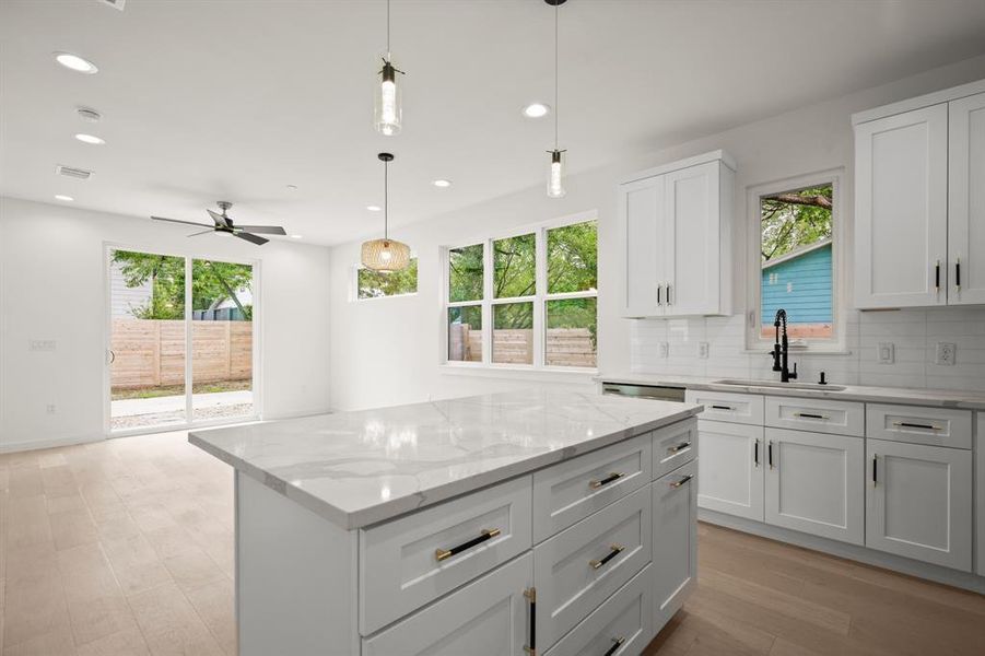 Kitchen featuring light wood-style flooring, decorative light fixtures, plenty of natural light, and light stone counters