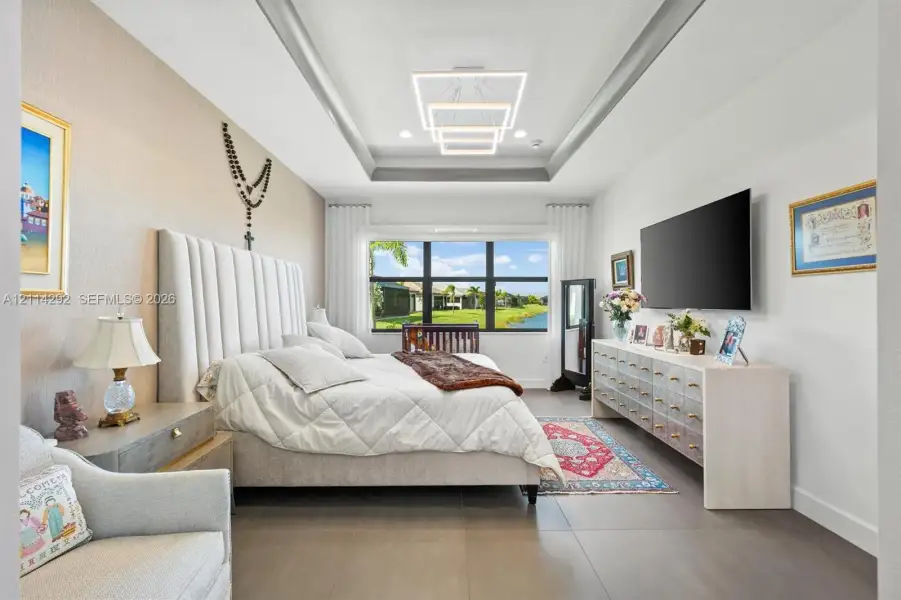 Tray ceiling featuring a geometric LED chandelier, large picture window, and neutral tile flooring