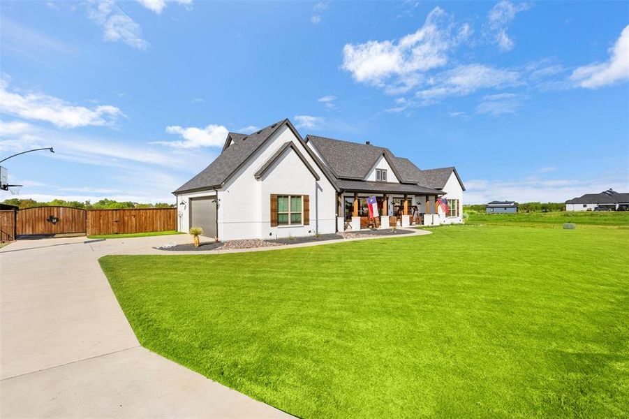 Modern inspired farmhouse featuring driveway, covered porch, an attached garage, a shingled roof, and a gate
