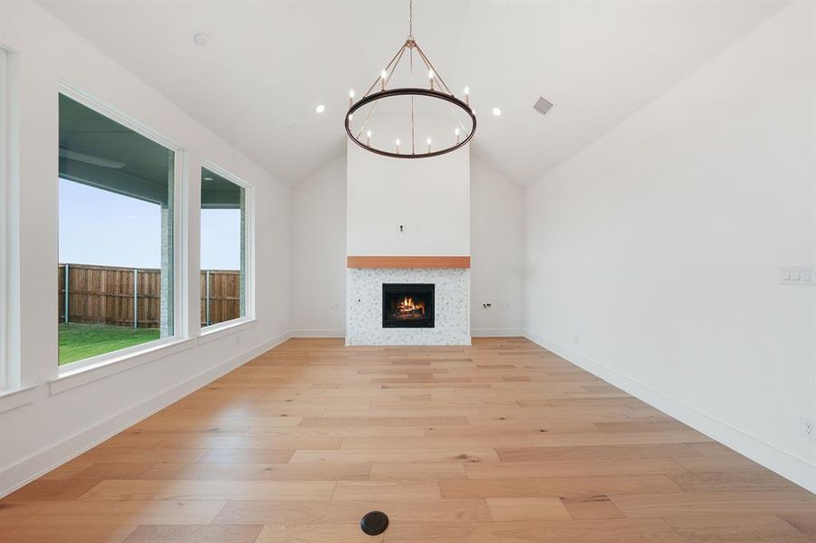 Unfurnished living room with light wood finished floors, a tile fireplace, a chandelier, high vaulted ceiling, and recessed lighting