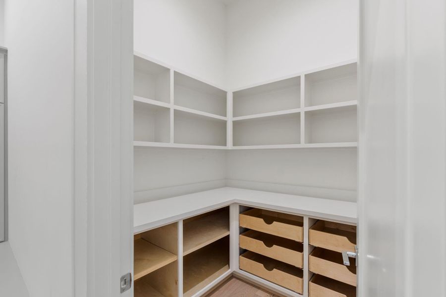A custom walk-in pantry is designed with built-in cabinetry, drawers, and shelving, providing both organization and a tailored, high-end feel.
