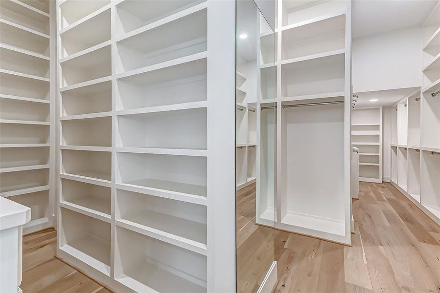 This spacious walk-in closet features ample shelving and hanging space, with a sleek, modern design and light wood flooring, perfect for organized storage.