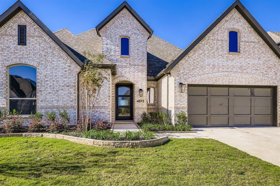 French country style house featuring brick siding, a front lawn, a shingled roof, driveway, and a garage French country style house featuring brick siding, a front lawn, a shingled roof, driveway, and a garage