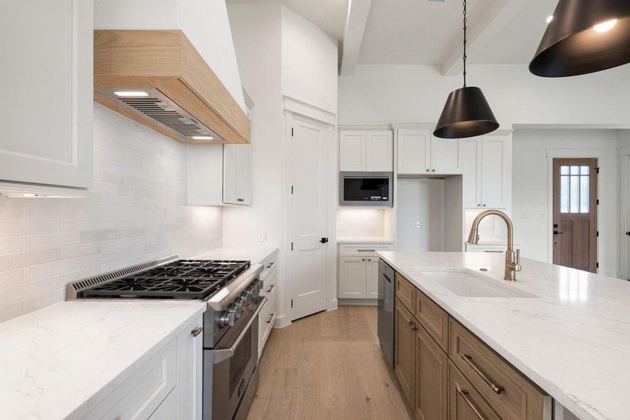 The kitchen features a gas range with a wooden range hood, white subway tile backsplash, and a large island with an integrated sink and dishwasher