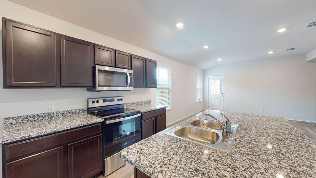 Kitchen featuring dark wood-finish cabinetry, light-toned countertops, and stainless steel appliances including a microwave and range