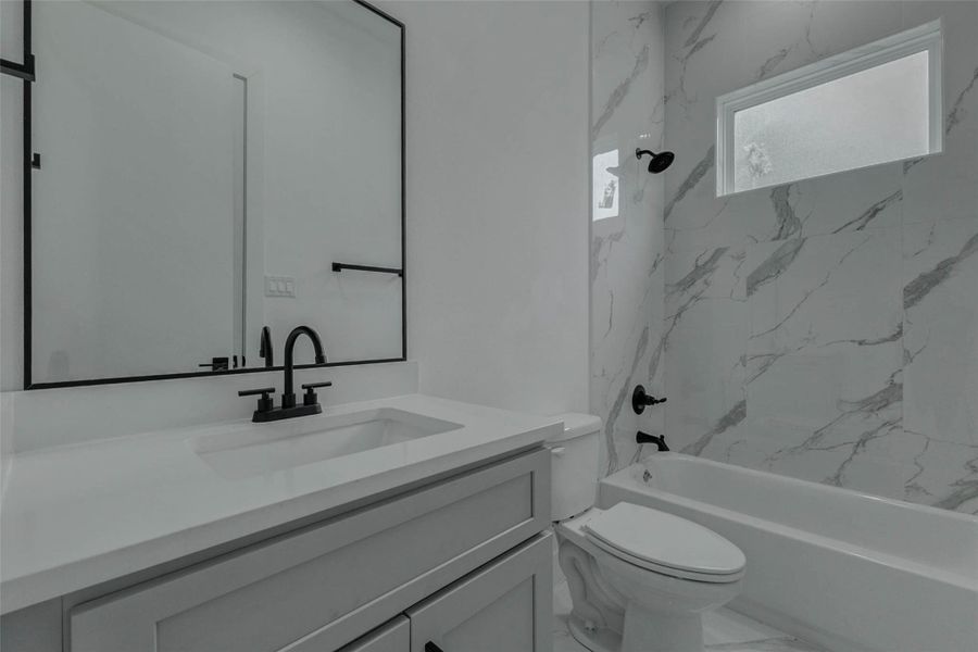 A closer look at the first-floor bathroom reveals marble-look wall tile, a tub-and-shower combination, black fixtures, and a clean glass enclosure. The crisp finishes create a polished bathroom for residents and overnight guests.