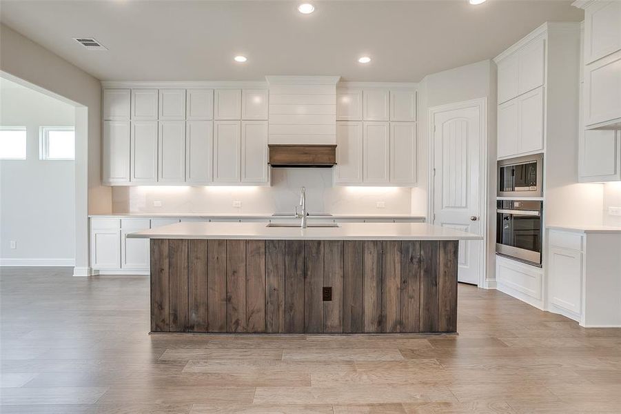 Kitchen featuring light hardwood / wood-style flooring, white cabinetry, a kitchen island with sink, and stainless steel appliances