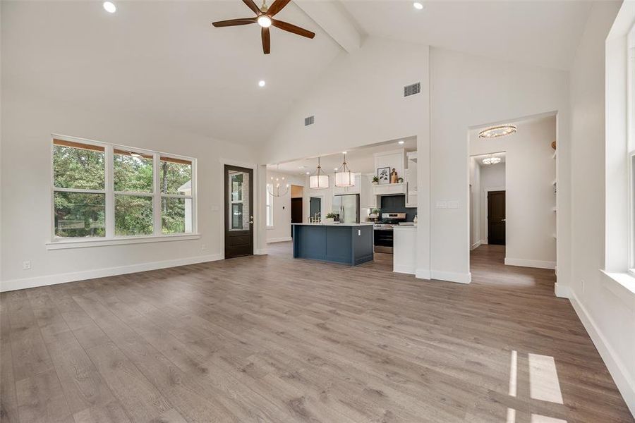 Unfurnished living room featuring high vaulted ceiling, light wood-style floors, beamed ceiling, a chandelier, and recessed lighting