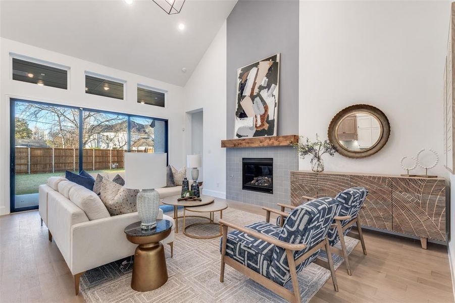Living area with light wood-type flooring, high vaulted ceiling, and a tiled fireplace Living area with light wood-type flooring, high vaulted ceiling, and a tiled fireplace