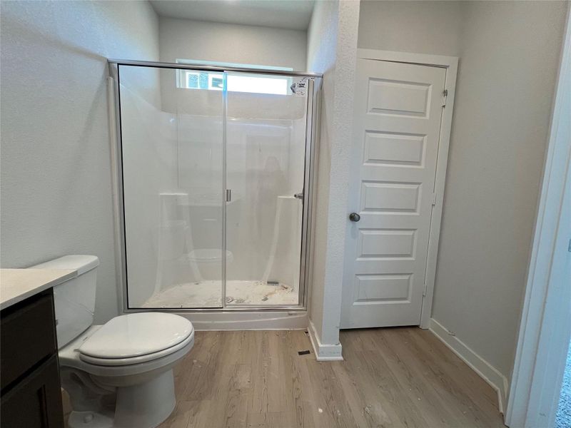 Bathroom with light wood-type flooring, a shower stall, vanity, and a textured wall
