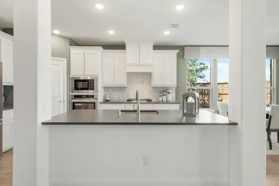 Kitchen with white cabinets, herringbone tile backsplash, dark countertop island, and stainless steel built-in appliances