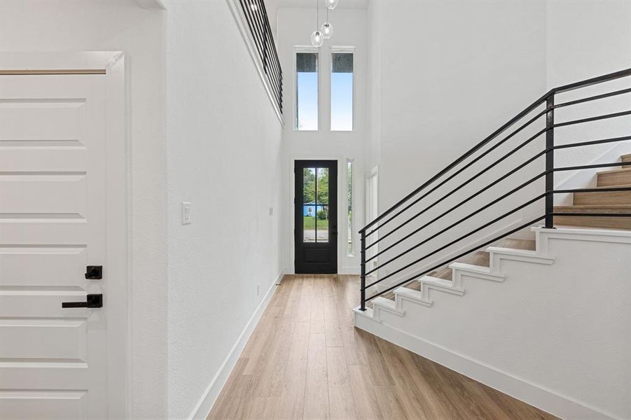 Entryway featuring light wood flooring, a black front door with glass panels, a staircase with black metal railings, and a contemporary chandelier Entryway featuring light wood flooring, a black front door with glass panels, a staircase with black metal railings, and a contemporary chandelier