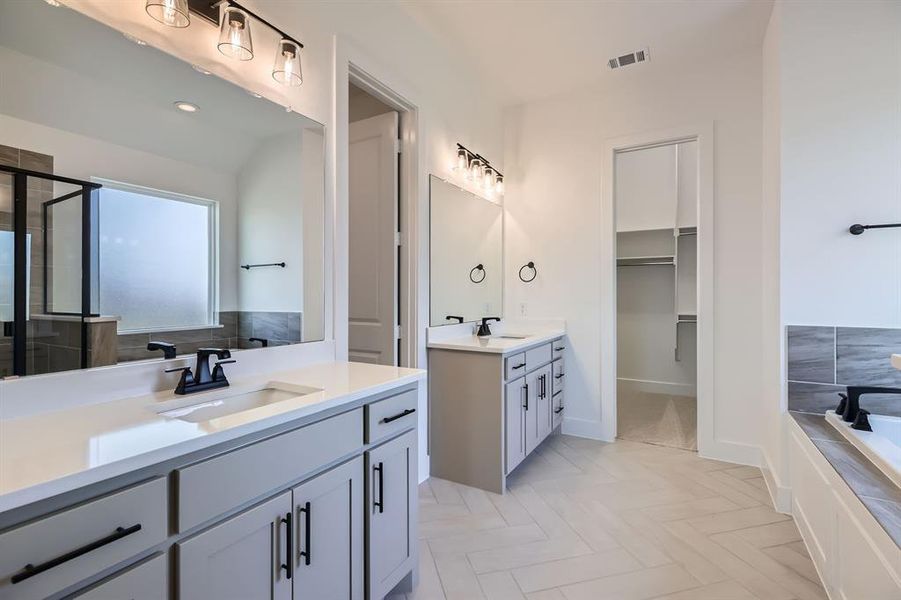 Full bathroom with two vanities, a bath, a shower stall, a walk in closet, and baseboards Full bathroom with two vanities, a bath, a shower stall, a walk in closet, and baseboards