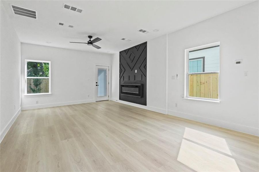 Unfurnished living room with a large fireplace, light wood-style floors, and ceiling fan